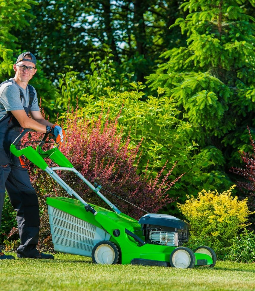 A man using a green lawn mower to mow a grassy lawn on a sunny day.