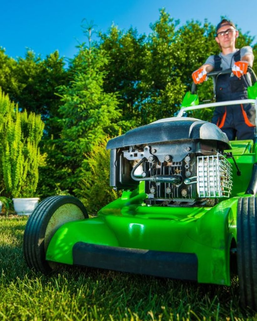 A man operates a green lawn mower, cutting grass in a well-maintained yard.